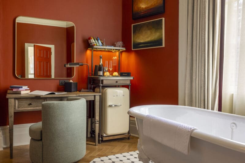 suite hotel room with red walls and free standing roll top bathtub
