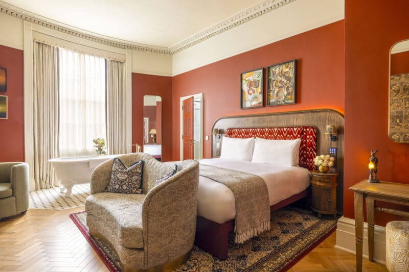 large suite in hotel with freestanding bathtub and red walls with a kingsize bed