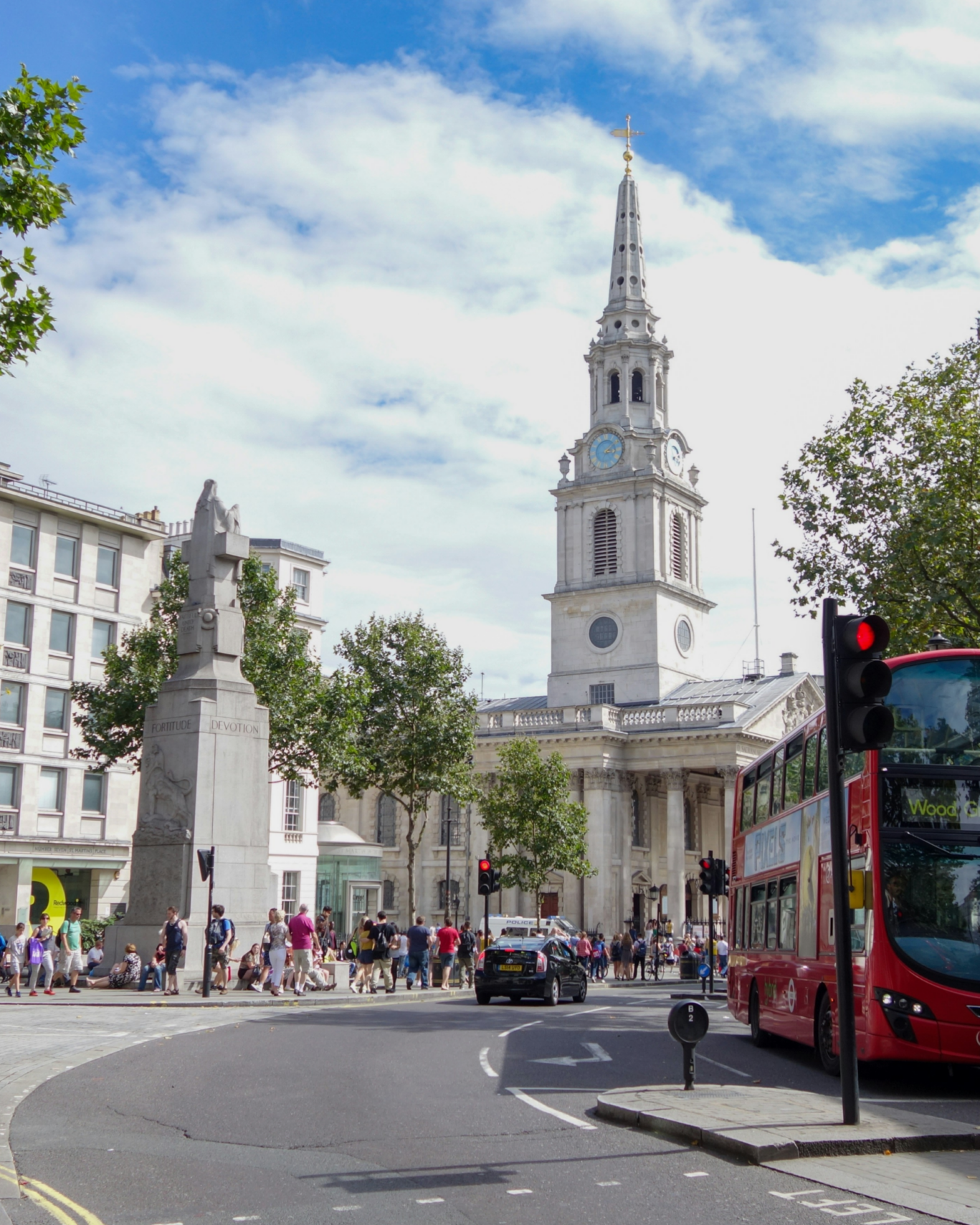 Leicester Square, featuring historic buildings, a red bus and many people on a warm, sunny and cloudy day.