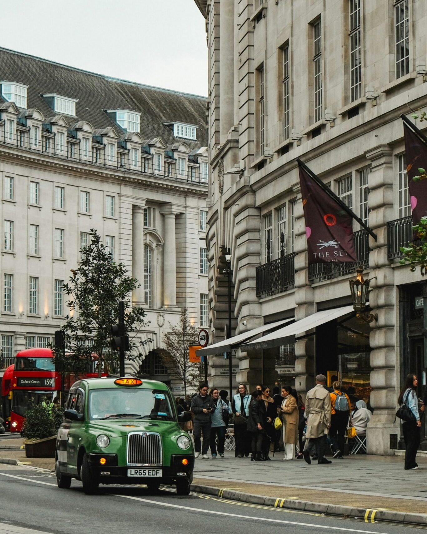 A green taxi cab drives along Oxford Street with grey buildings.