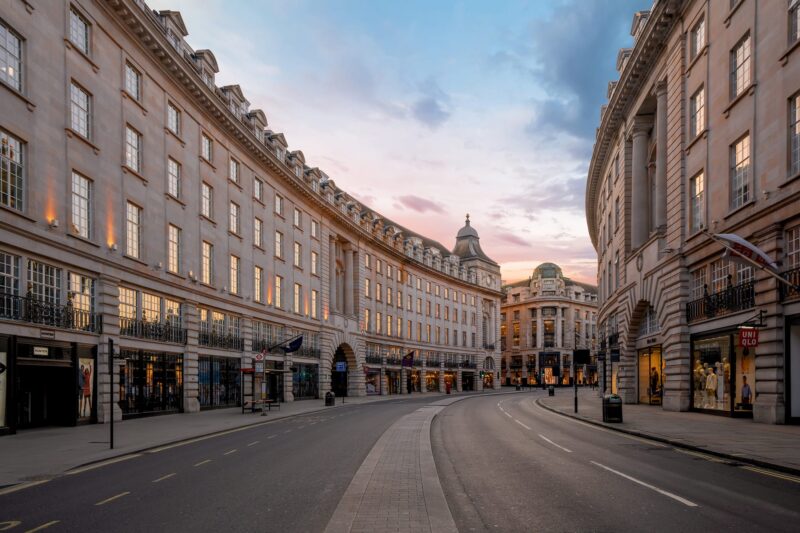 Regent street at twilight. The streets are empty, shops closed with lights on and red and orange hues sit in the sky.