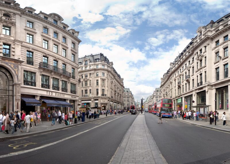 The bustling streets of Oxford Circus with lots of people walking and several buses in view on a bright sunny day.