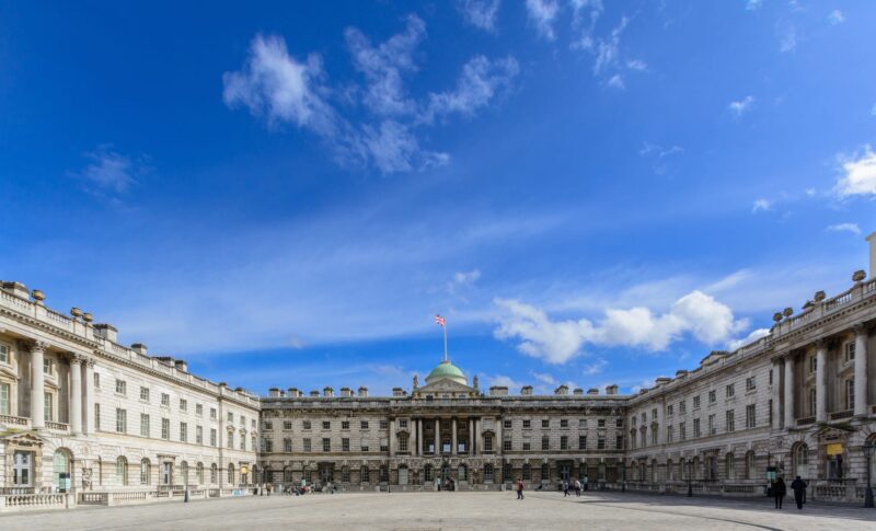 A huge square surrounded by Somerset House on a bright sunny day with wispy clouds in the sky.