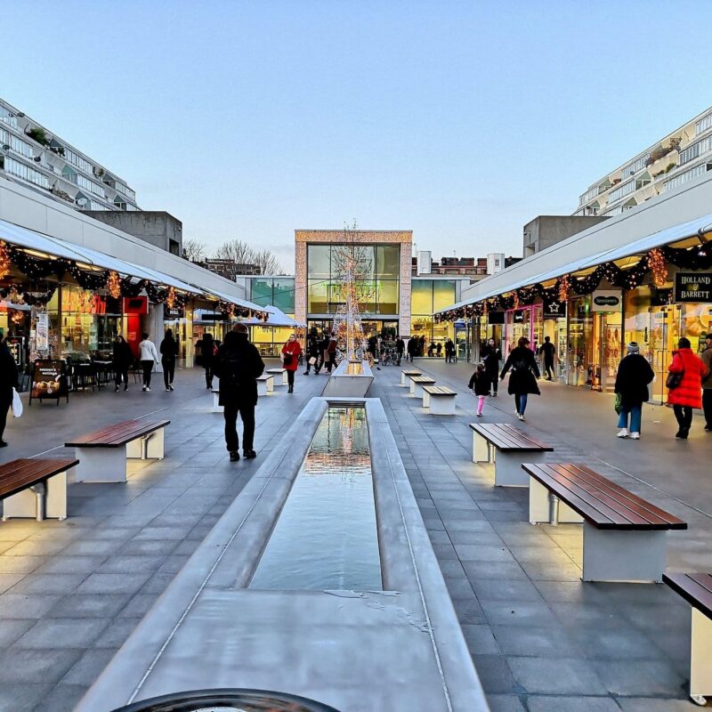 A selection of shops in the Brunswick Centre on a light winter's day with lights glowing.